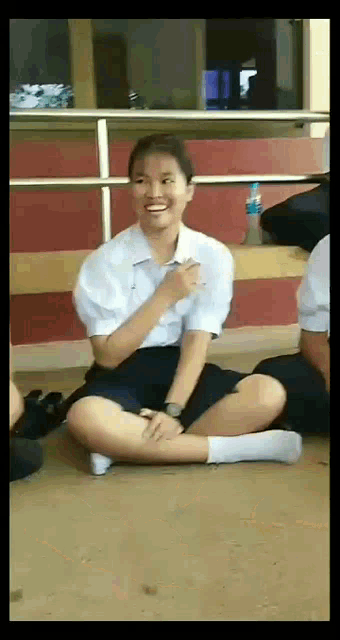 a girl in a school uniform is sitting on the floor and smiling