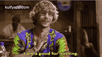 a man in a colorful shirt is sitting at a table and says i am a good for nothing .