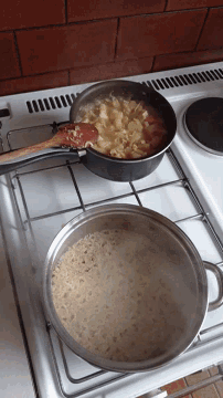 two pots of food are cooking on a stove with a wooden spoon in one of them