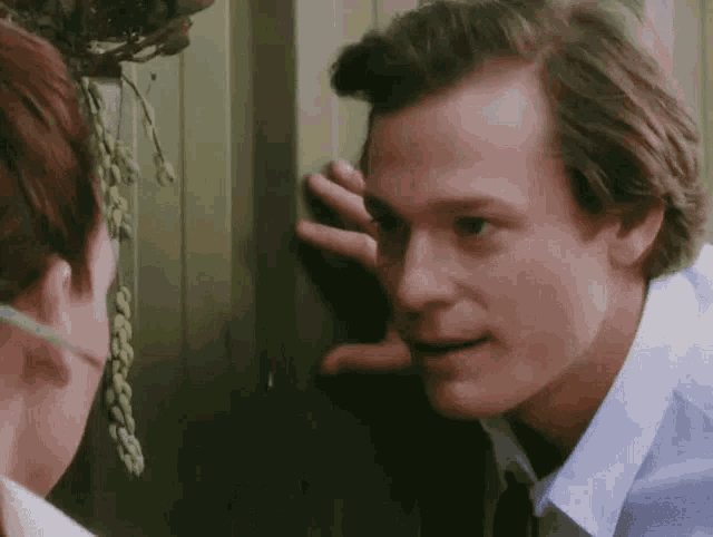 a man is peeking into a woman 's ear while a woman looks on .