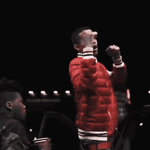 a man in a red jacket is singing into a microphone while another man watches .