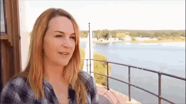 a woman in a plaid shirt is standing on a balcony overlooking a lake .