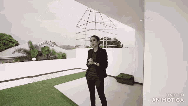 a woman in a black suit is standing in front of a white wall with the words made in animatica on the bottom