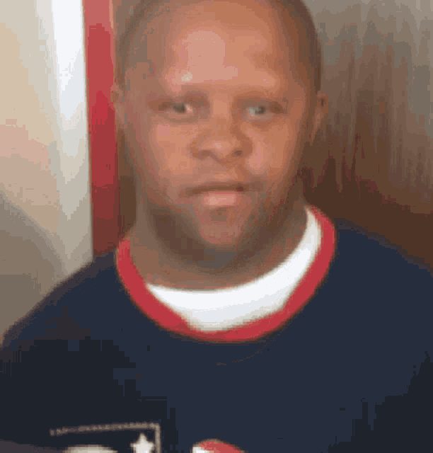 a man wearing a blue shirt with a red white and blue star on it looks at the camera