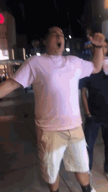 a man wearing a pink shirt and khaki shorts is standing on a sidewalk with his arms outstretched
