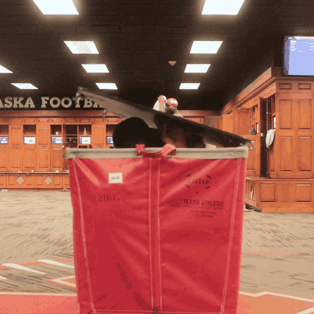 a red laundry bag in a locker room with a sign above it that says alaska football