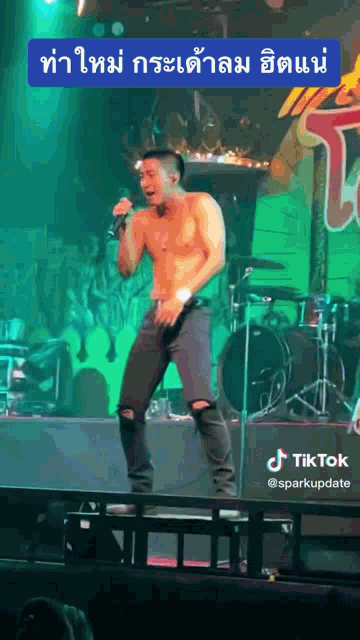 a shirtless man is singing into a microphone on a stage with a tiktok logo behind him