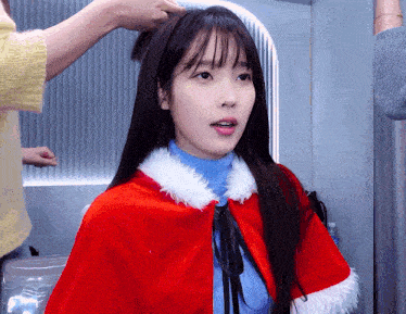 a woman wearing a red cape and a blue sweater is getting her hair done