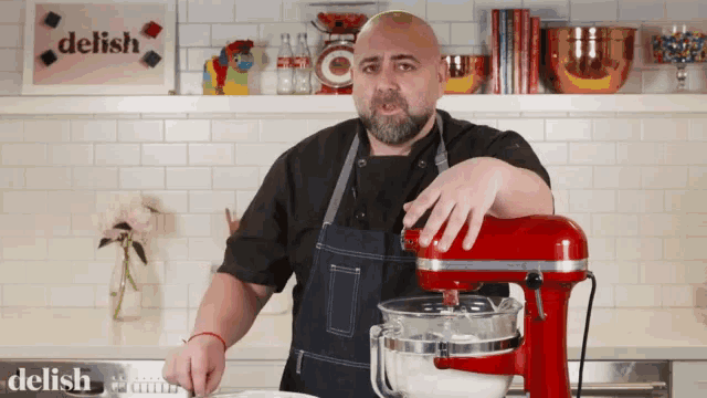 a man is standing in front of a red mixer with a delish sign behind him