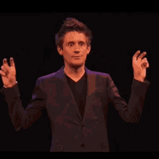 a man in a suit is standing on a stage with his arms outstretched and making a funny face .