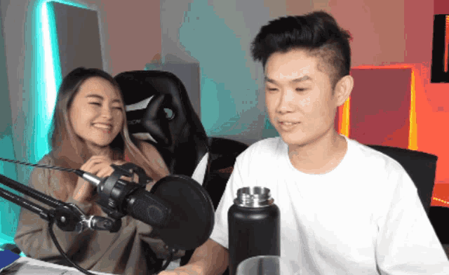 a man and a woman are sitting in front of a microphone with a black water bottle in front of them