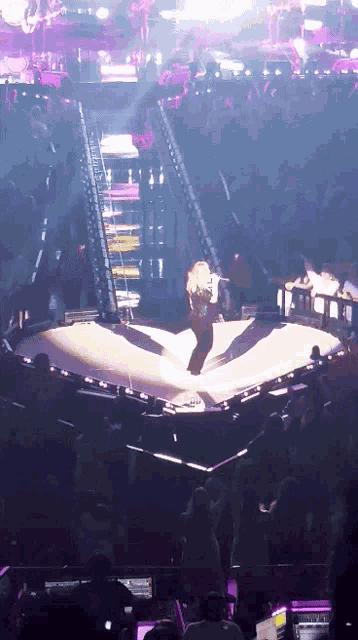 a woman is standing on a stage in front of a crowd with a purple light behind her