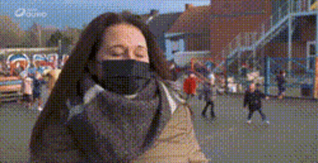a woman wearing a black mask and a scarf is standing in front of a crowd of people .