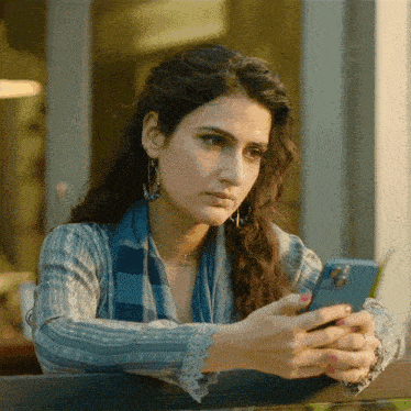 a woman in a blue sweater looks at her cell phone
