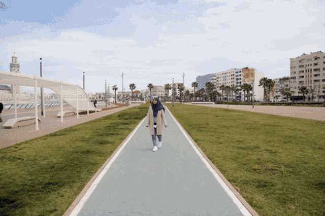 a woman wearing a hijab is walking down a path in a park