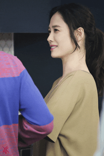 a woman in a ponytail smiles while standing next to another woman