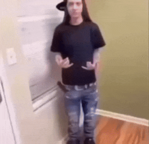 a man with long hair is standing in a kitchen .