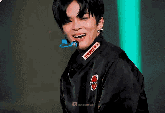 a young man wearing a black jacket with the word treasure on it is smiling .