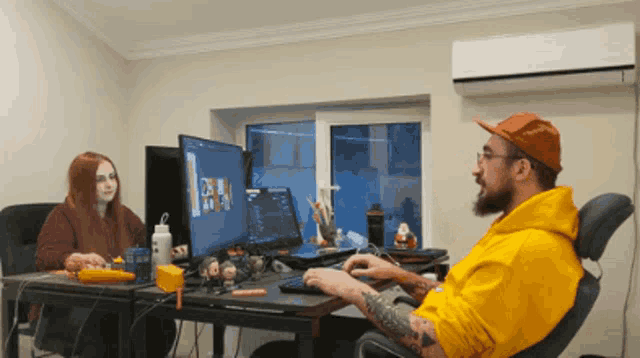 a man in a yellow hoodie sits in front of a computer screen