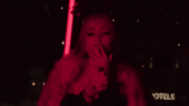 a woman is smoking a cigarette in a dark room with red lights behind her .