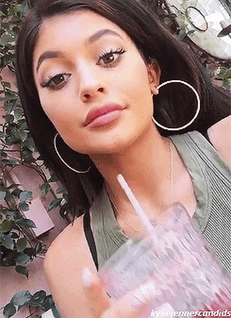 a close up of a woman wearing hoop earrings and drinking from a glass