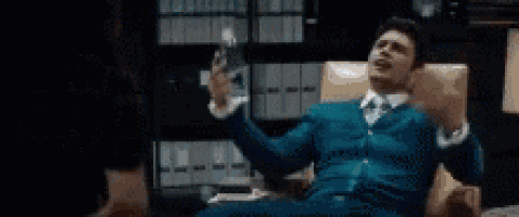 a man in a suit and tie is sitting in a chair holding a glass of wine and screaming .