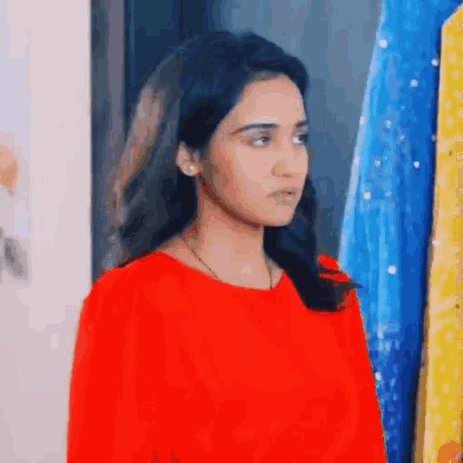 a woman in a red shirt is standing in front of a row of clothes .