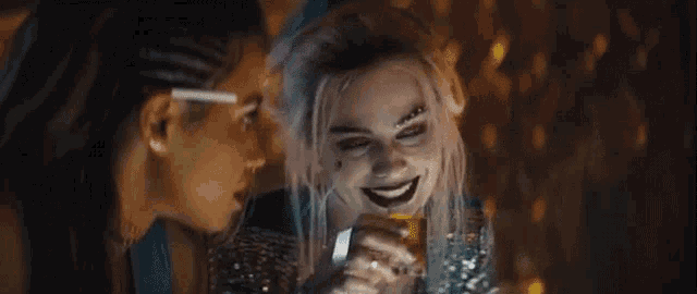 two women are sitting next to each other in a dark room . one of the women is wearing a joker costume .