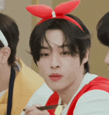 a young man wearing a red bunny ear headband is eating with chopsticks .