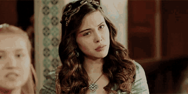 a woman with a necklace and a tiara on her head looks at the camera