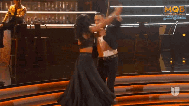 a man and a woman are dancing on a stage with a mqb logo in the corner
