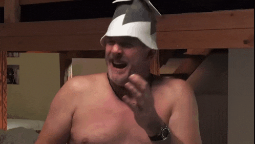 a shirtless man wearing a hat and a watch laughs