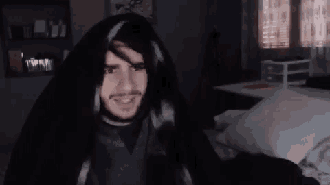 a man with a beard is sitting in a chair in a dark room with a blanket on his head .