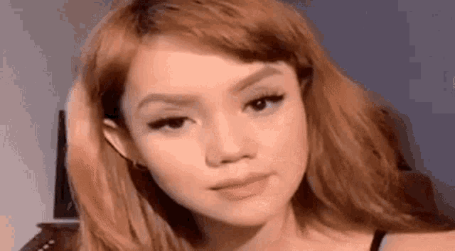 a close up of a woman 's face with red hair and a black top .