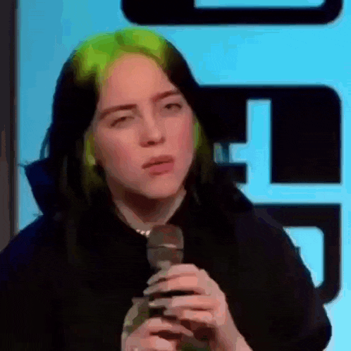 billie eilish is holding a microphone in front of a blue background .