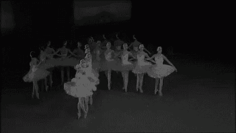 a black and white photo of a group of ballerinas dancing in a dark room .