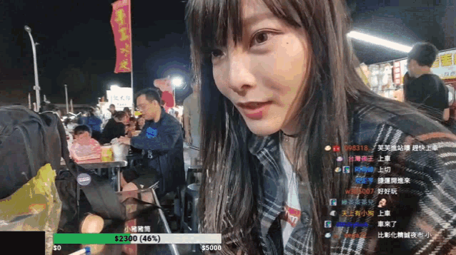 a woman in a plaid shirt is looking at the camera while a man sits at a table in the background ..