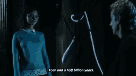 a man and a woman are standing next to each other in a dark room and the woman is wearing a blue sweater .