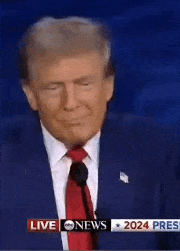 a man in a suit and tie is giving a speech in front of a live abc news banner