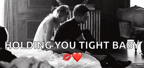 a man and a woman are sitting on a bed with the words holding you tight baby above them