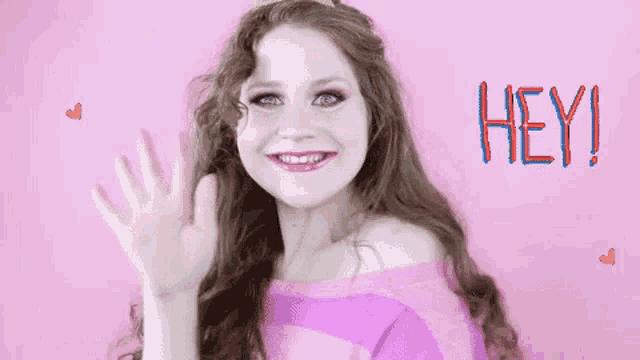 a woman in a pink sweater is waving her hand in front of the word hey