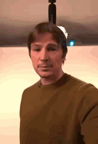 a man in a brown sweater is taking a selfie with a tripod on his head .