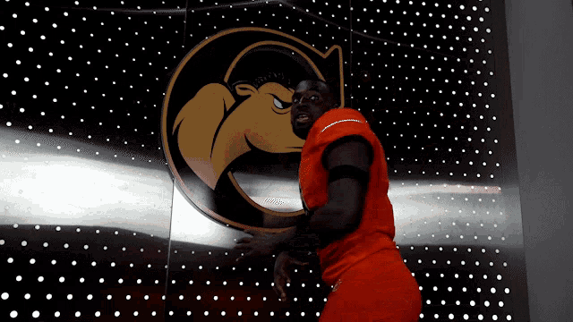 a man in an orange jersey is standing in front of a wall with a g on it