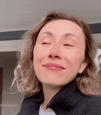 a woman in a black jacket is smiling with her eyes closed