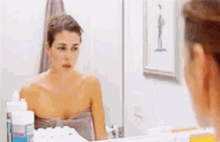 a woman wrapped in a towel is looking at herself in a bathroom mirror