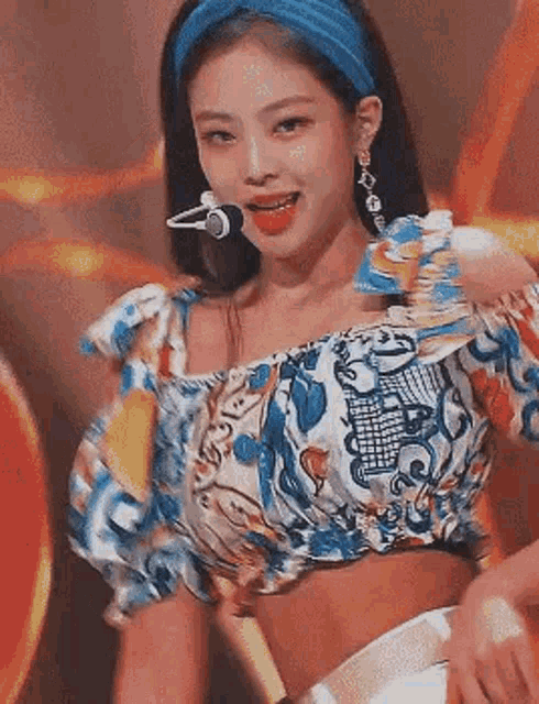 blackpink jennie is wearing a blue headband and a crop top while singing into a microphone .