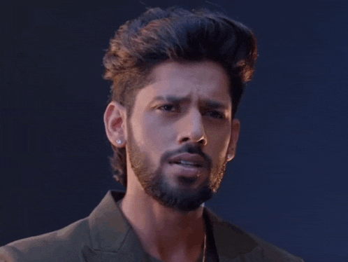 a man with a beard and earrings is looking at the camera with a serious look on his face .