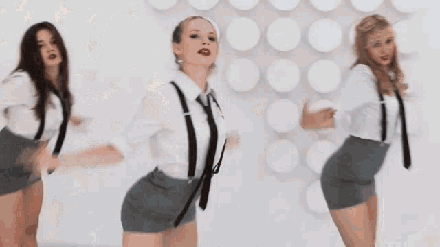three women in school uniforms and ties are dancing in front of a white wall