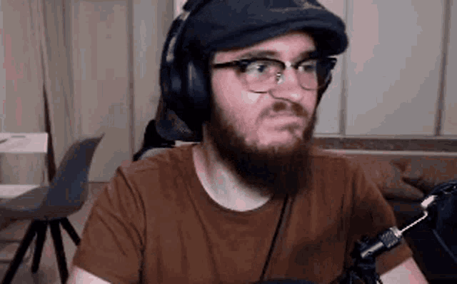 a man with a beard wearing headphones and a hat is sitting in front of a microphone .