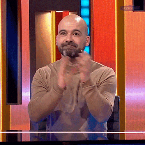 a bald man with a beard is clapping his hands in front of a red wall